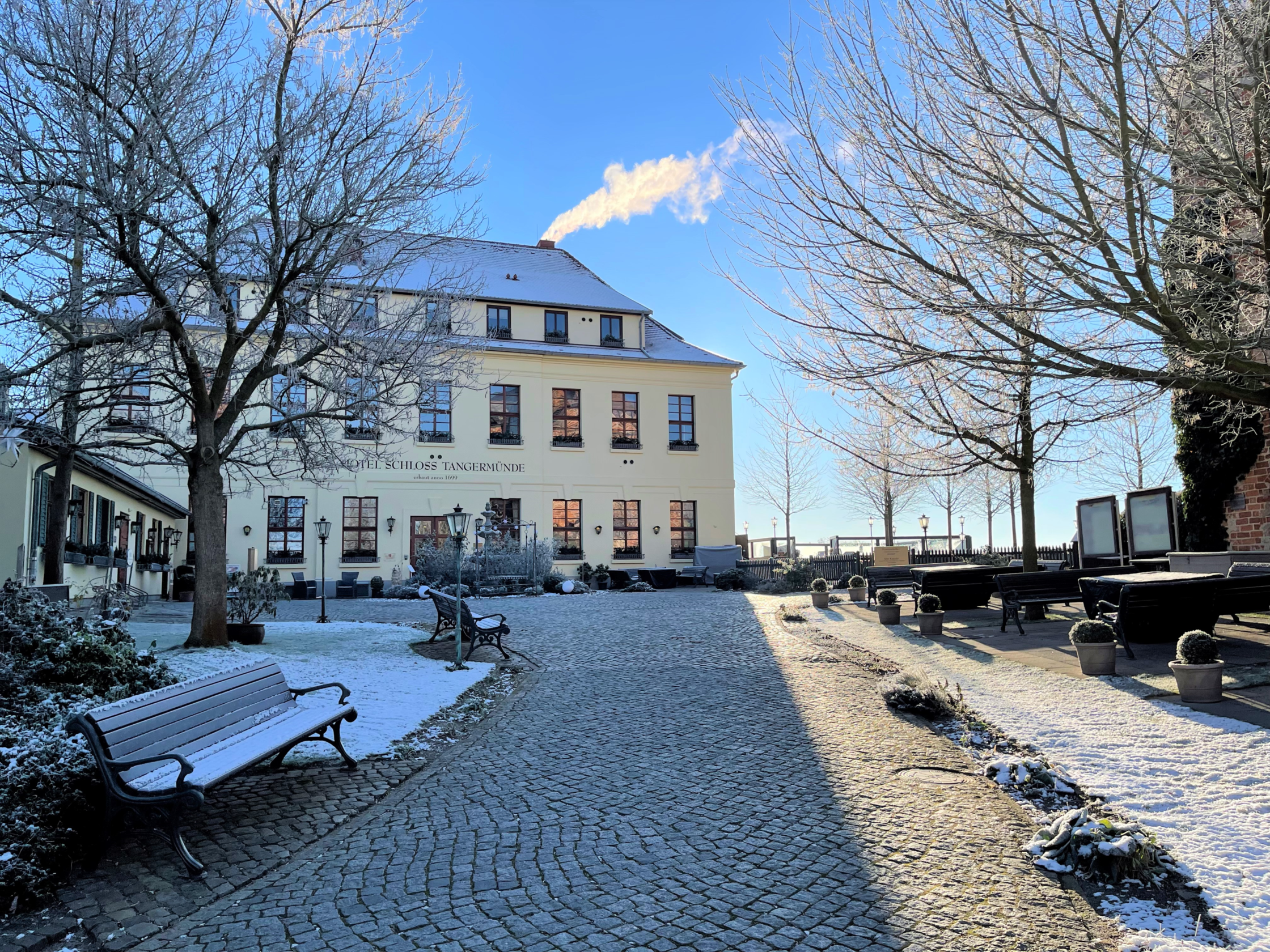 Hauptgebäude des Hotel Schloss Tangermünde im Winter.  Schnee/ Reif liegt auf dem Hoteldach und der Bank sowie dem Rasen.